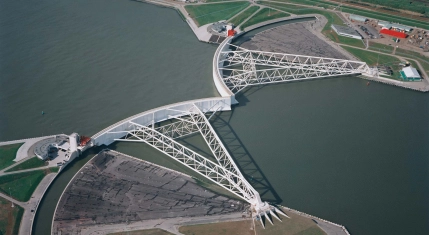 Luchtfoto van de Maeslantkering in Hoek van Holland met de gesloten keringarmen en omliggende waterbouwkundige infrastructuur.
