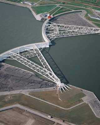 Luchtfoto van de Maeslantkering in Hoek van Holland met de gesloten keringarmen en omliggende waterbouwkundige infrastructuur.